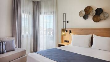 Habitación de hotel con una cama grande, una mesita de noche, un sofá y cortinas traslúcidas.
