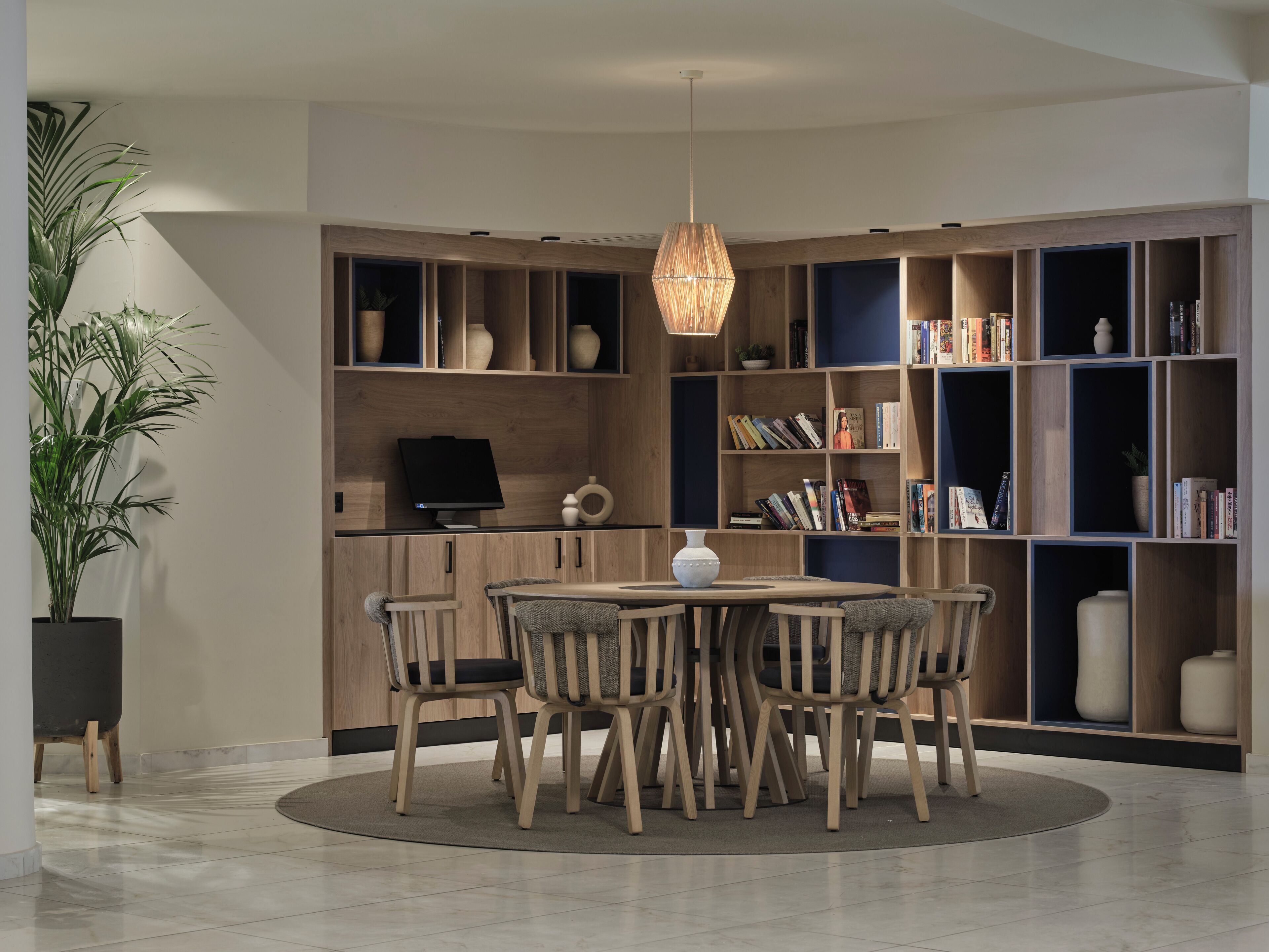 A modern library with a round table and chairs, wooden bookshelves, and a hanging light fixture.