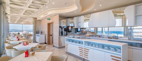 A modern restaurant with a central counter, seating area, and a view of the sea.