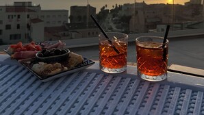 Une table garnie de plats et de boissons, une vue sur le coucher de soleil et des immeubles de la ville en arrière-plan.
