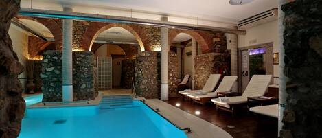 A swimming pool with stone arches, lounge chairs, and a stone pillar.