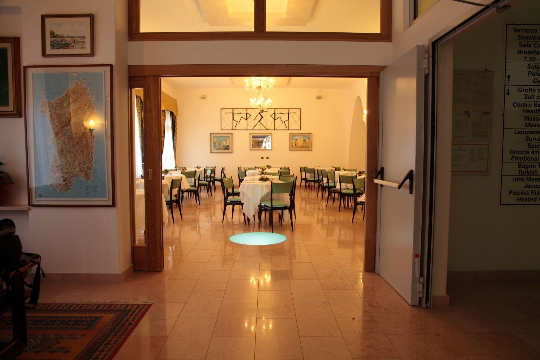 A hotel lobby with a dining area, a chandelier, framed artwork, and a map on the wall.