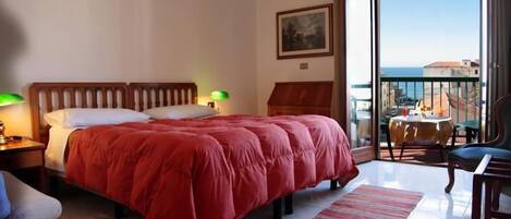 A hotel room with a large bed, a balcony with a table and chairs, and a view of the sea.