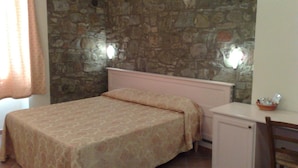 Une chambre à coucher avec un lit, une petite armoire et un mur en pierre.