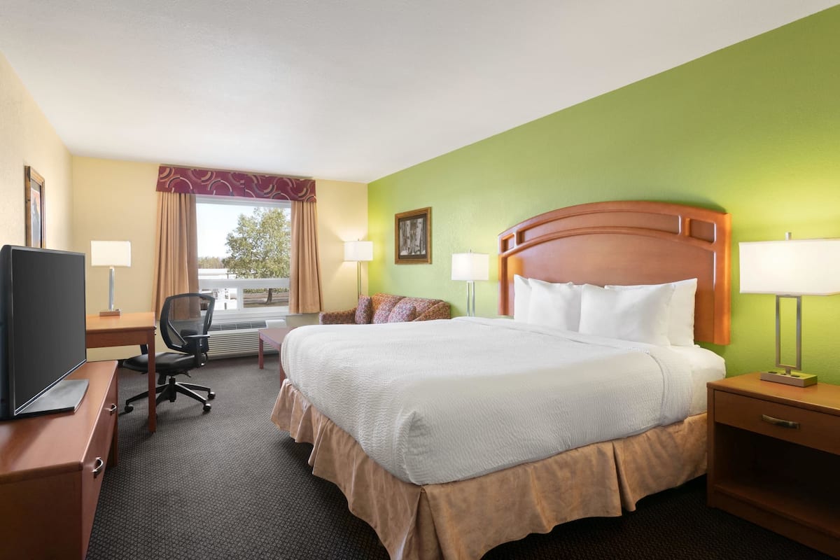 A hotel room with a bed, desk, chair, TV, and a window with curtains.