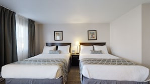 A hotel room with two beds, a nightstand with a lamp, and two framed pictures on the wall. - Dilworth Inn (Kelowna)
