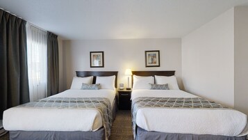 A hotel room with two beds, a nightstand with a lamp, and two framed pictures on the wall.