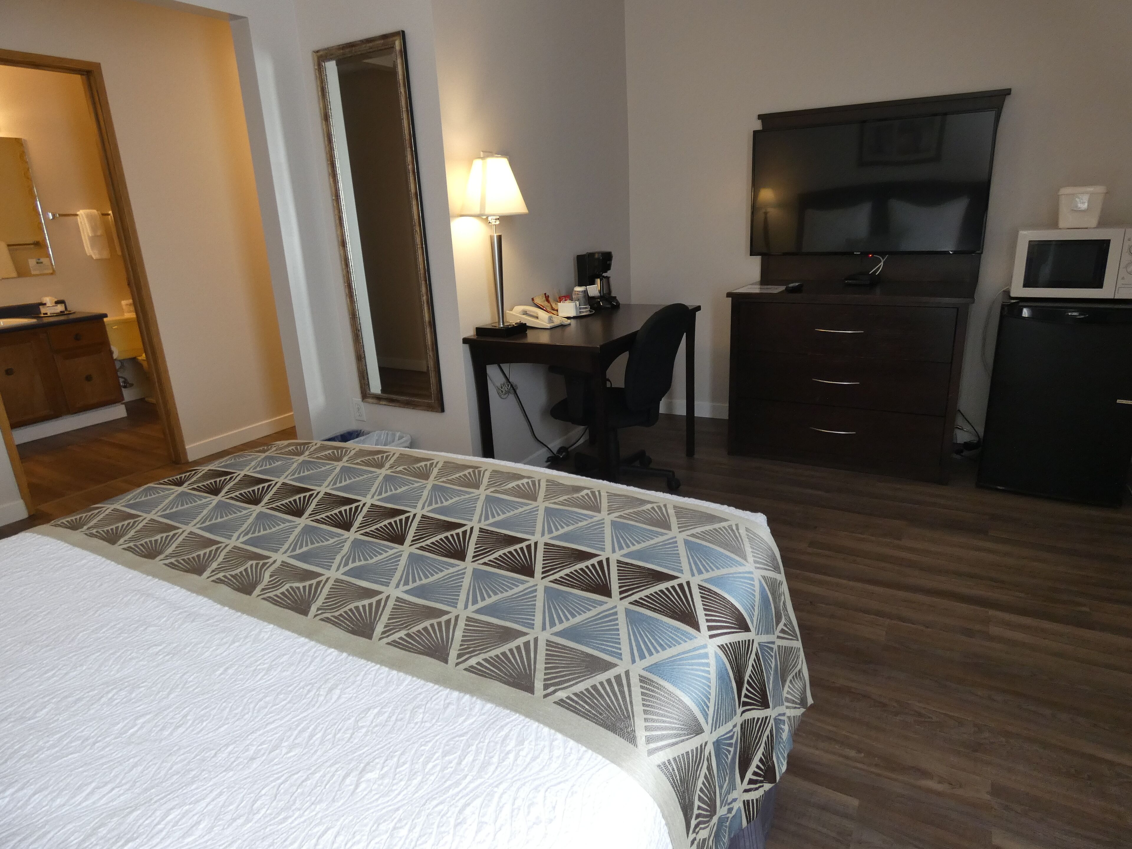 Une chambre d’hôtel équipée d’un lit, d’un bureau, d’une chaise, d’une télévision, d’un four à micro-ondes et d’une commode.
