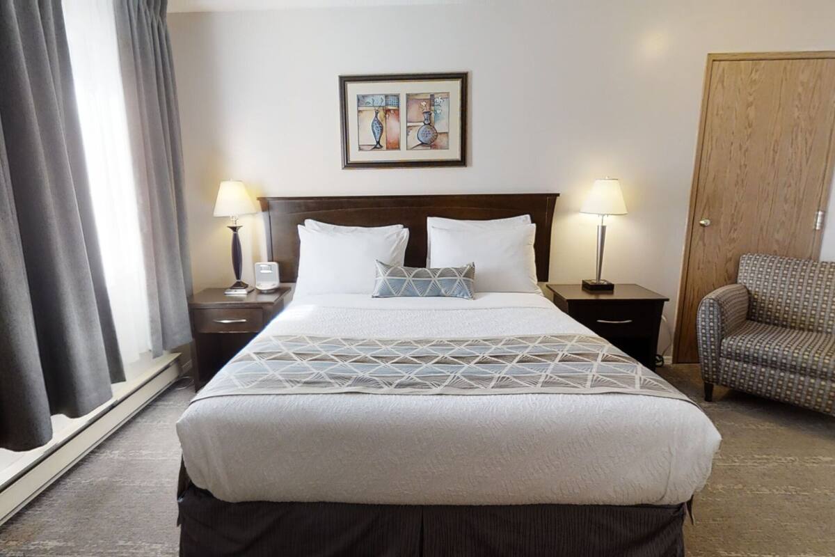 Una habitación de hotel con una cama grande, dos mesitas de noche con lámparas, una silla y una puerta.