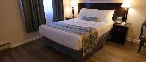Una habitación de hotel con una cama grande, dos mesitas de noche con lámparas, un cuadro enmarcado sobre la cama y una ventana con cortinas.