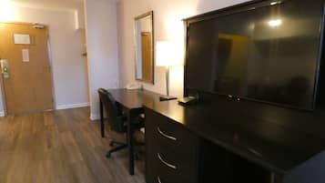 A hotel room with a desk, chair, and a large flat-screen TV.