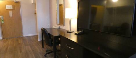A hotel room with a desk, chair, and a large flat-screen TV.