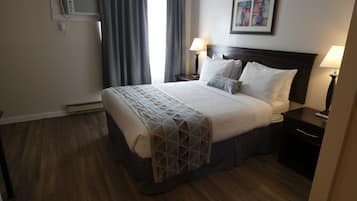 Ein Hotelzimmer mit einem Bett, zwei Nachttischen mit Lampen, einer Wandklimaanlage und einem gerahmten Bild an der Wand.
