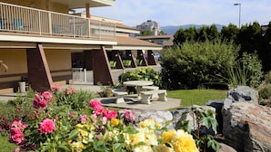 A building with a balcony, outdoor seating, and a garden with flowers and rocks. - Dilworth Inn (Kelowna)