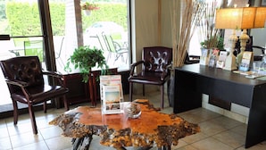 A reception area with a wooden coffee table, leather chairs, a desk with brochures, and a view of the outdoors through large windows. - Dilworth Inn (Kelowna)