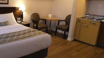 Habitación de hotel con cama, dos sillas, una mesita, escritorio y kitchenette.