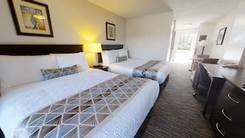 Habitación de hotel con dos camas, un escritorio y una silla. Se observan cuadros en las paredes y una lámpara en la mesita de noche.