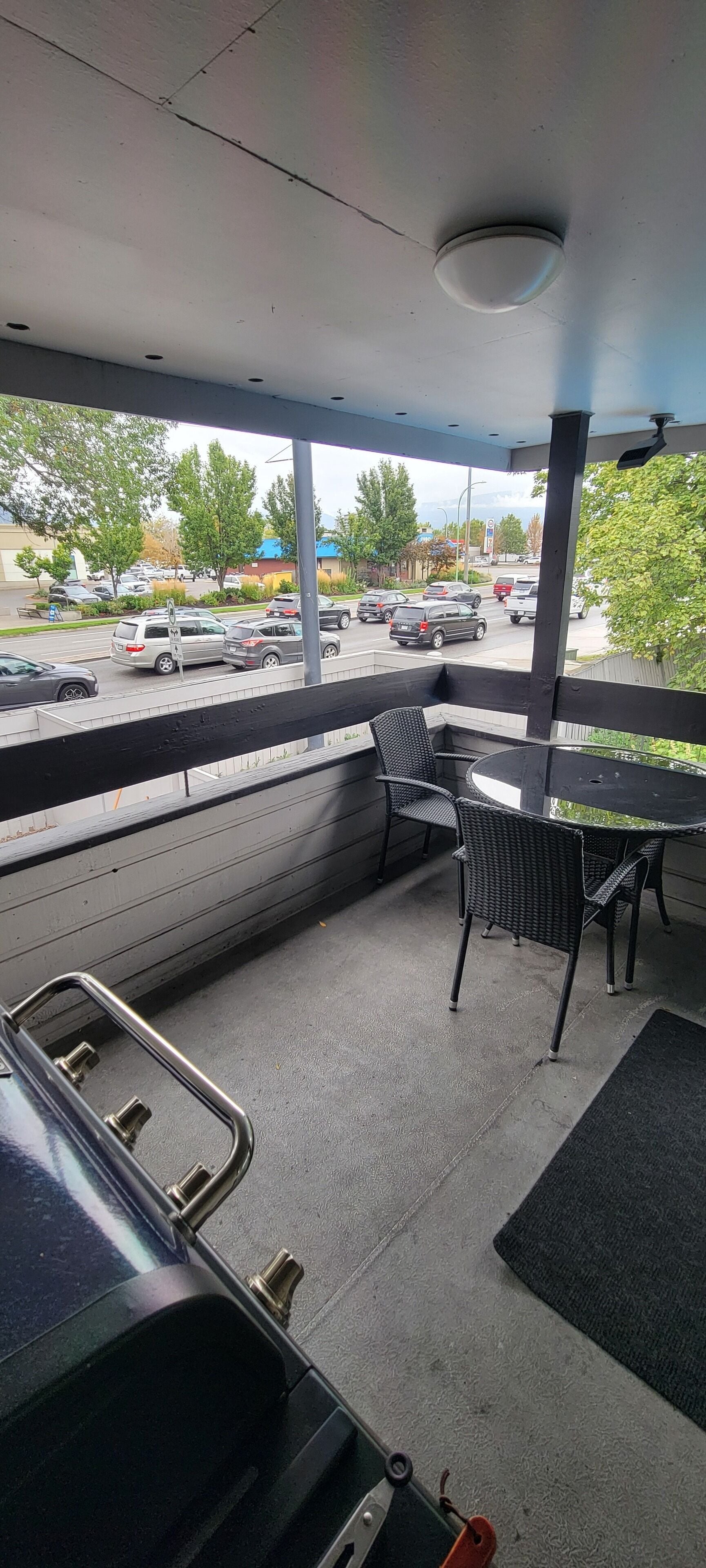 A covered outdoor seating area with a table and chairs, a view of a parking lot, and a ceiling-mounted light fixture.