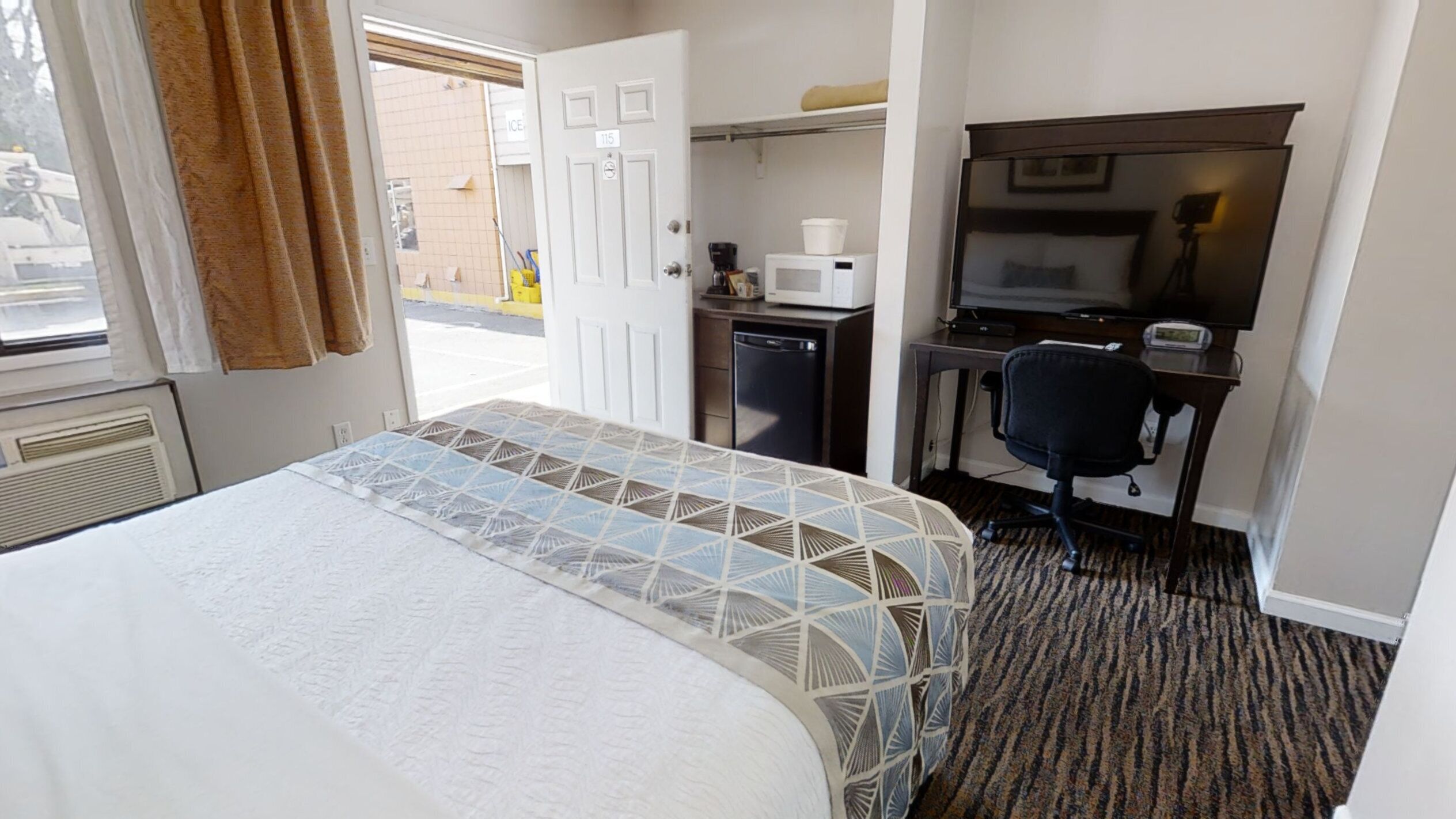 Habitación de hotel con cama, escritorio, silla, microondas y un pequeño refrigerador.