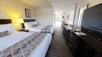 A hotel room with two beds, a desk, a television, and a window.