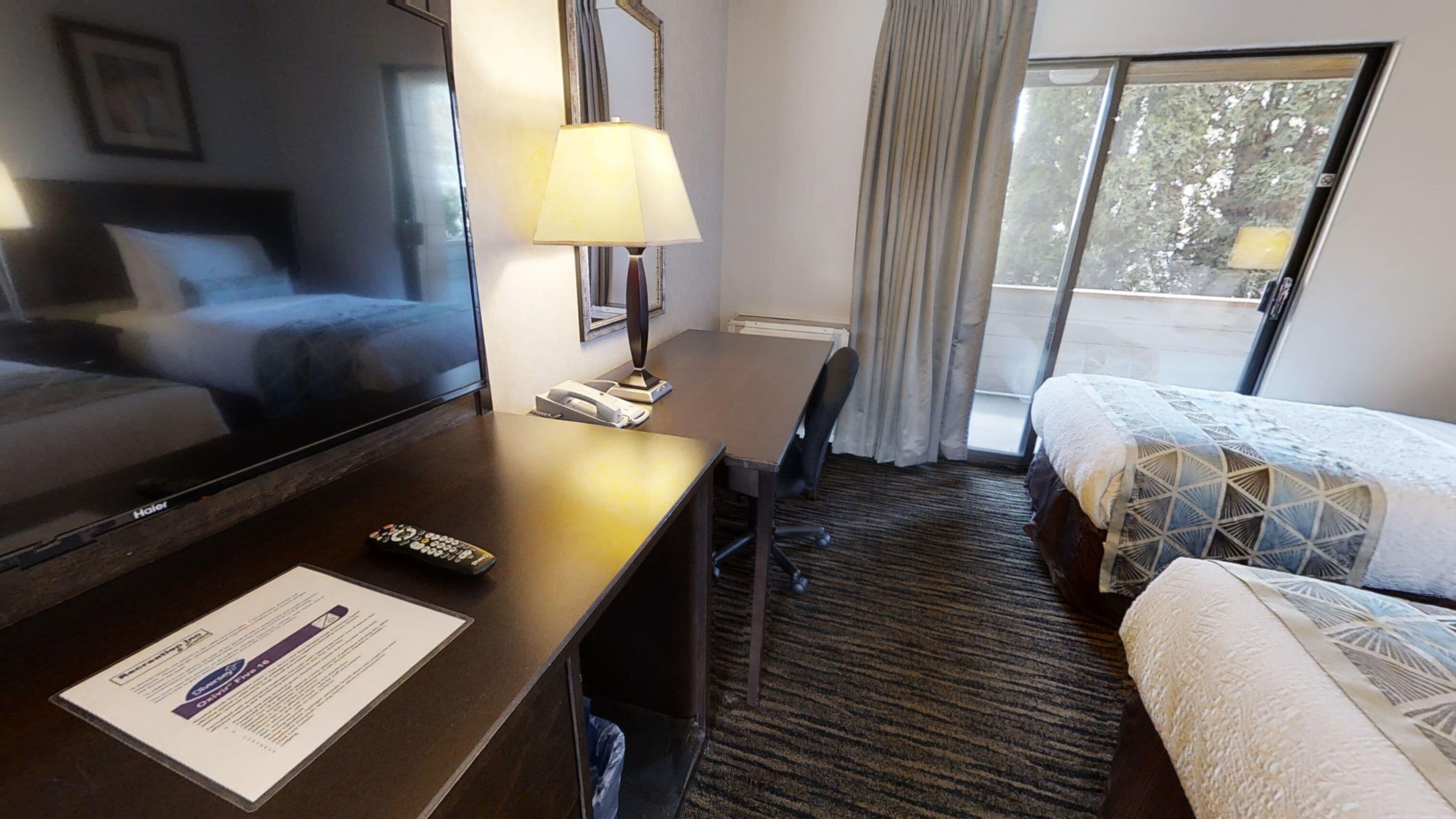 A hotel room with a bed, a desk with a lamp, a chair, a TV, and a window with curtains.