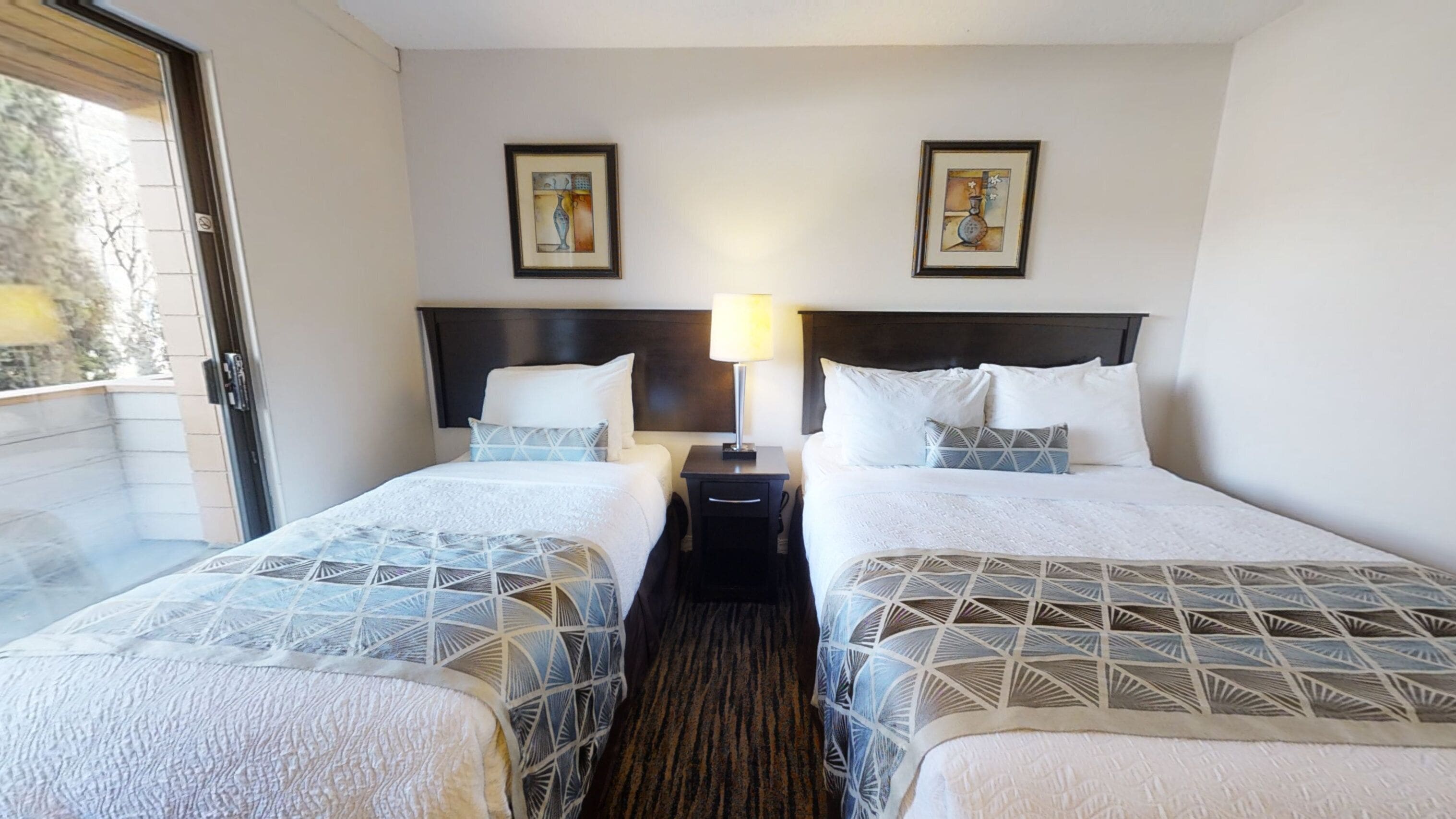 Une chambre d’hôtel avec deux lits, une table de chevet avec une lampe et deux œuvres d’art encadrées accrochées au mur.