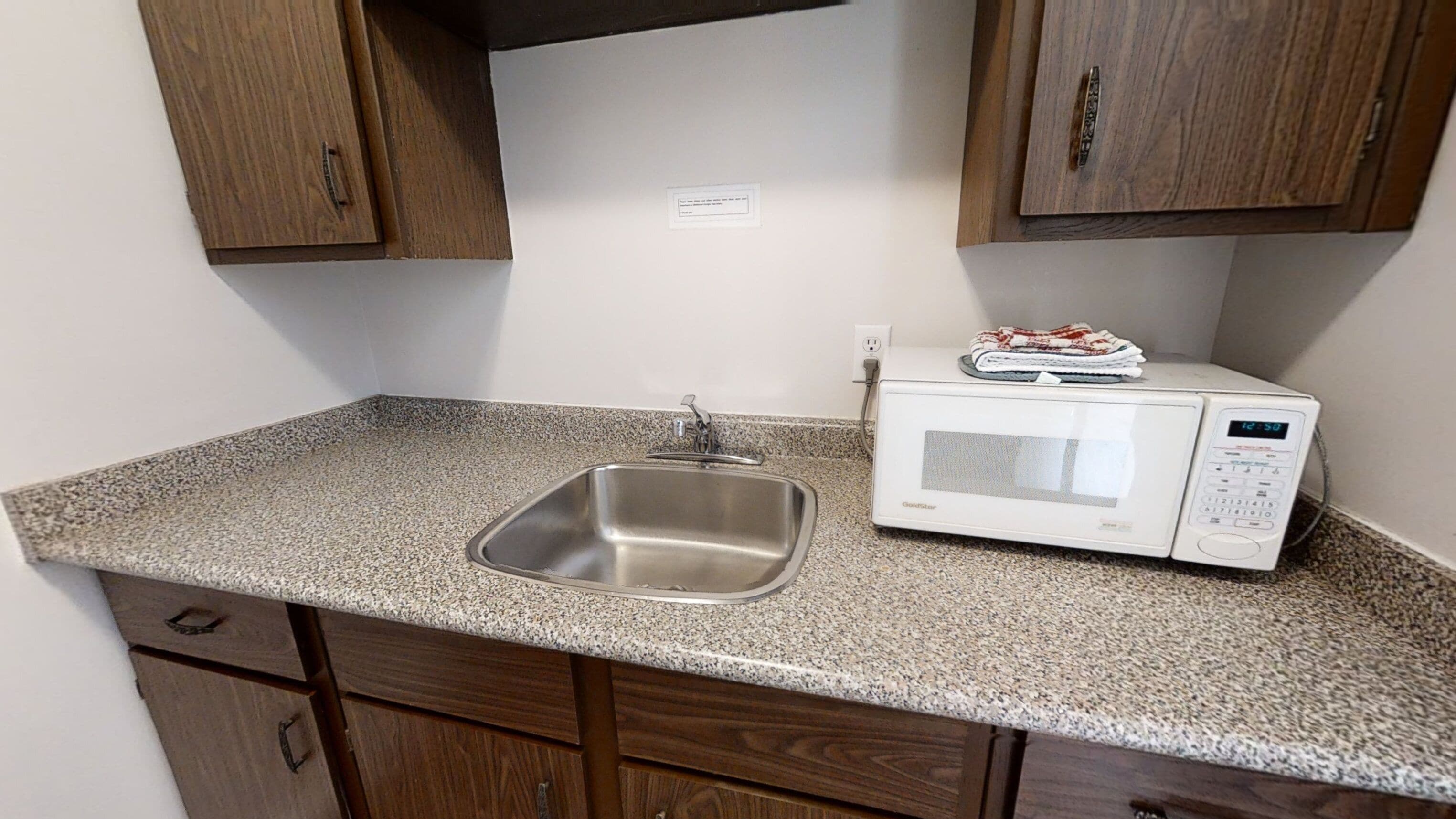 A kitchen with a granite countertop, stainless steel sink, and a white microwave.