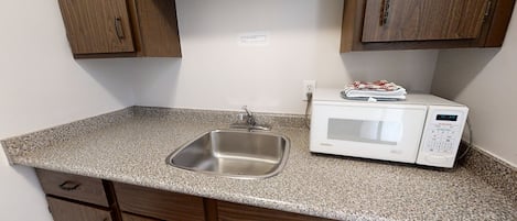 A kitchen with a granite countertop, stainless steel sink, and a white microwave.