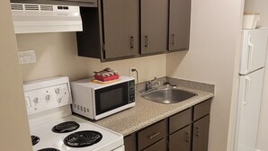 A compact kitchen with dark cabinets, a white stove, a microwave, and a sink. - Recreation Inn & Suites (Kelowna)