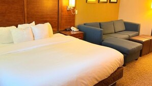 Une chambre d’hôtel avec un grand lit, un canapé, une table de chevet avec un téléphone et une lampe fixée au mur.