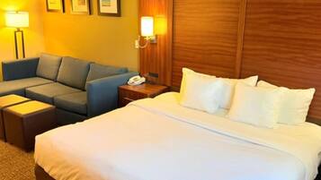 Una habitación de hotel con cama, sofá, mesita de noche con teléfono y lámparas de pared.