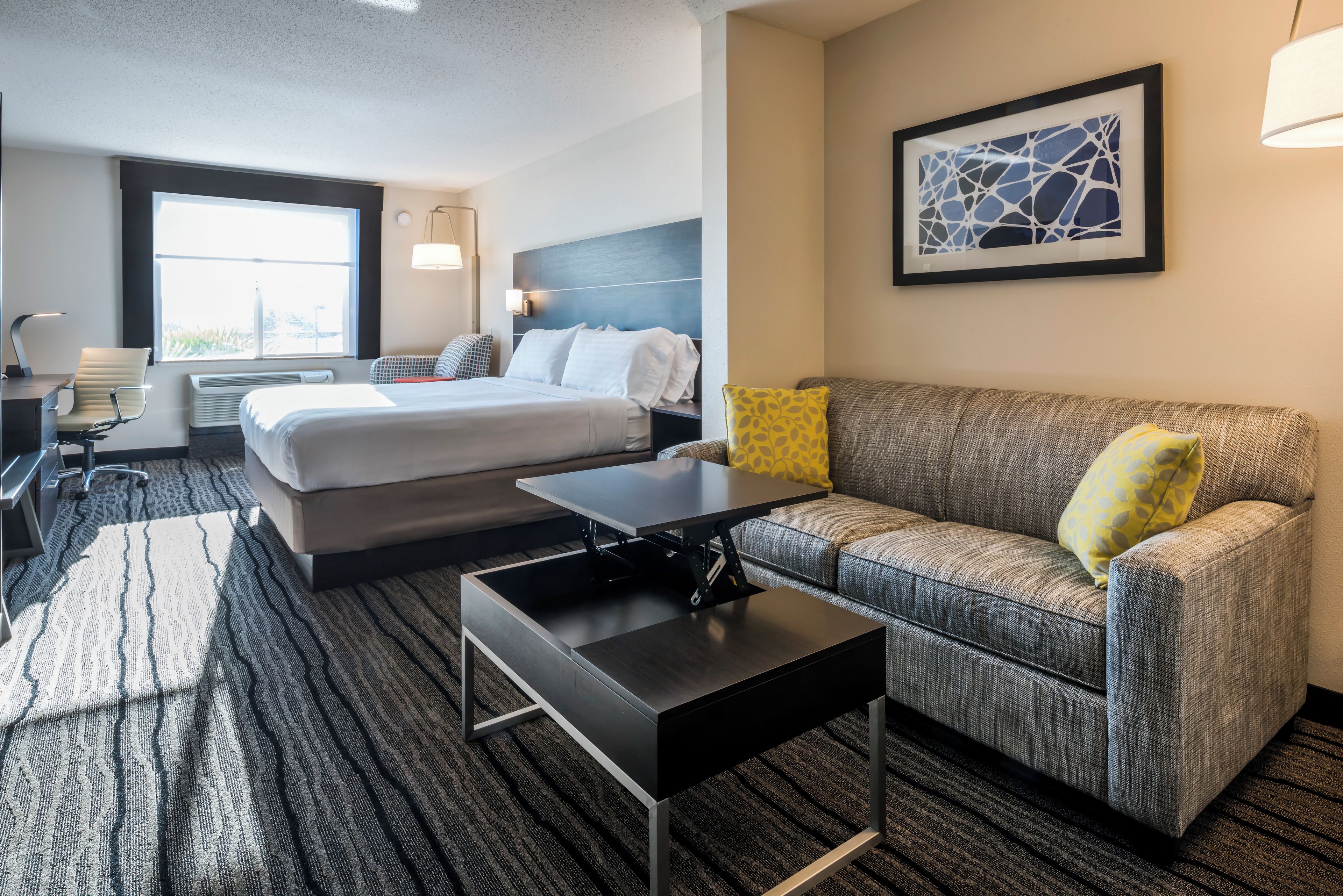 A hotel room with a bed, a sofa, a desk, and a window.