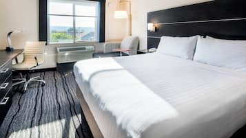 Habitación de hotel con una cama grande, un escritorio con silla, una mesita, una lámpara y una ventana con vistas.