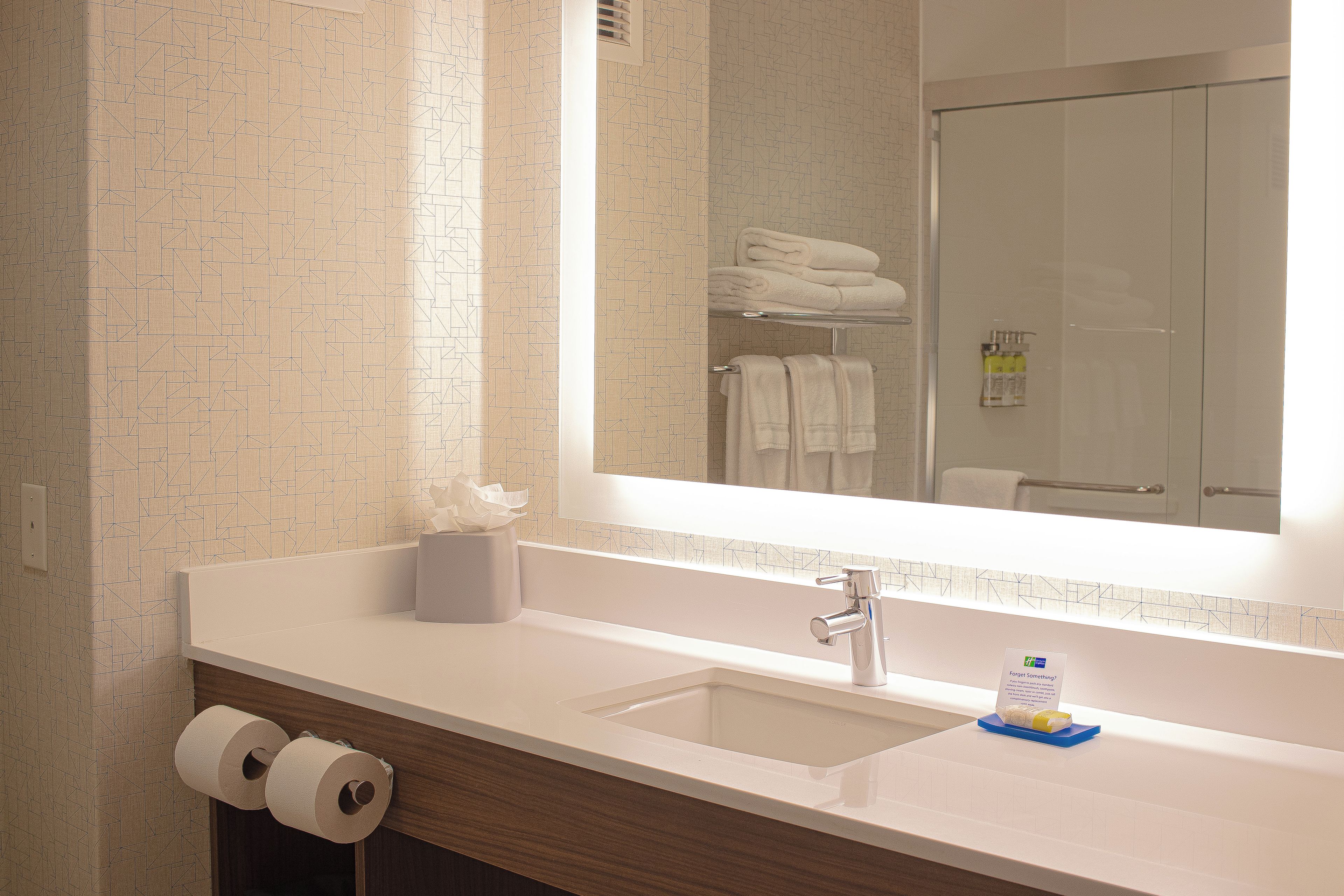 Ein Badezimmer mit Waschbecken, Spiegel, Handtuchhalter und Toilettenpapier.