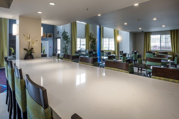 A spacious indoor area with multiple tables and chairs, large windows with curtains, and potted plants. - Holiday Inn Express Hotel & Suites Livermore by IHG (Livermore)