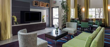 A hotel lobby with a flat-screen TV, seating area, and large windows.