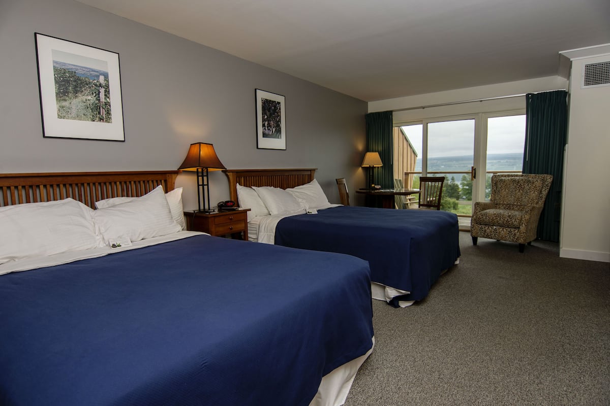 A hotel room with two beds, a chair, a table, and a large window with a view.