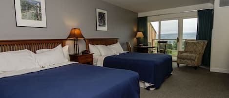 Habitación de hotel con dos camas, una silla, una mesa y un ventanal con vistas.