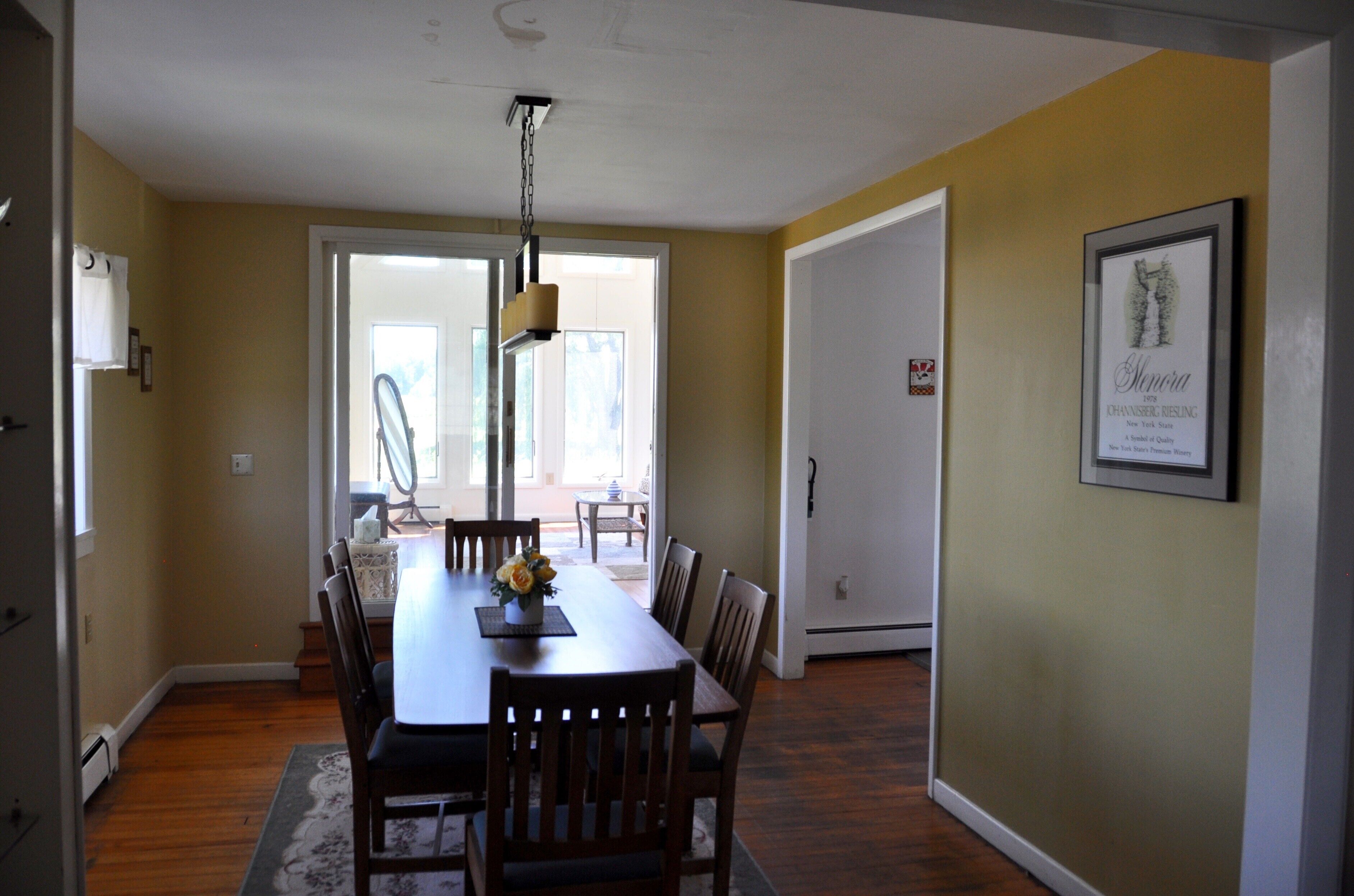 A dining room with a wooden table and chairs, a chandelier, and a framed picture on the wall.