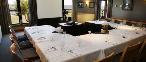 A conference room with multiple tables set for dining, equipped with wine glasses and napkins.