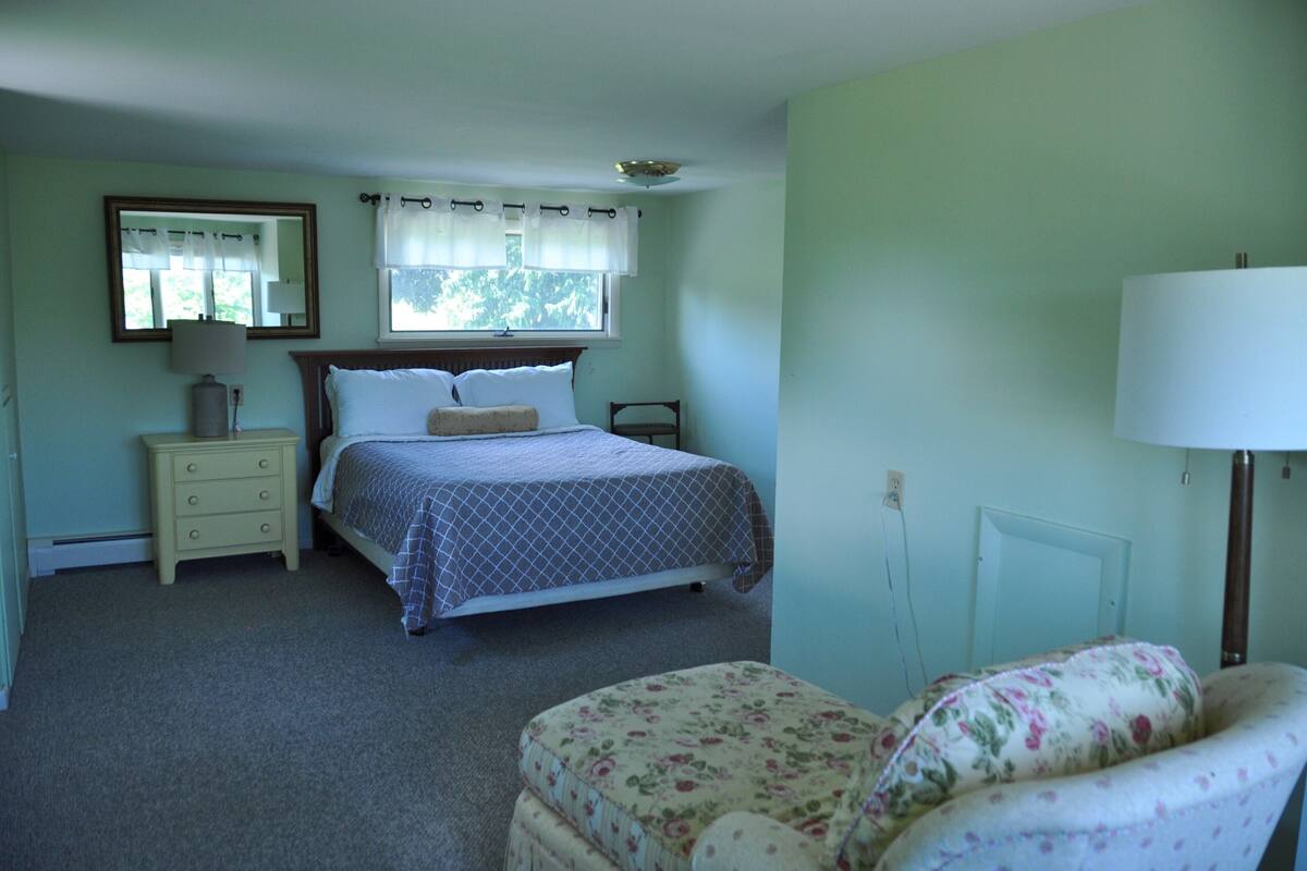 A bedroom with a bed, nightstand, chair, and a window with curtains.
