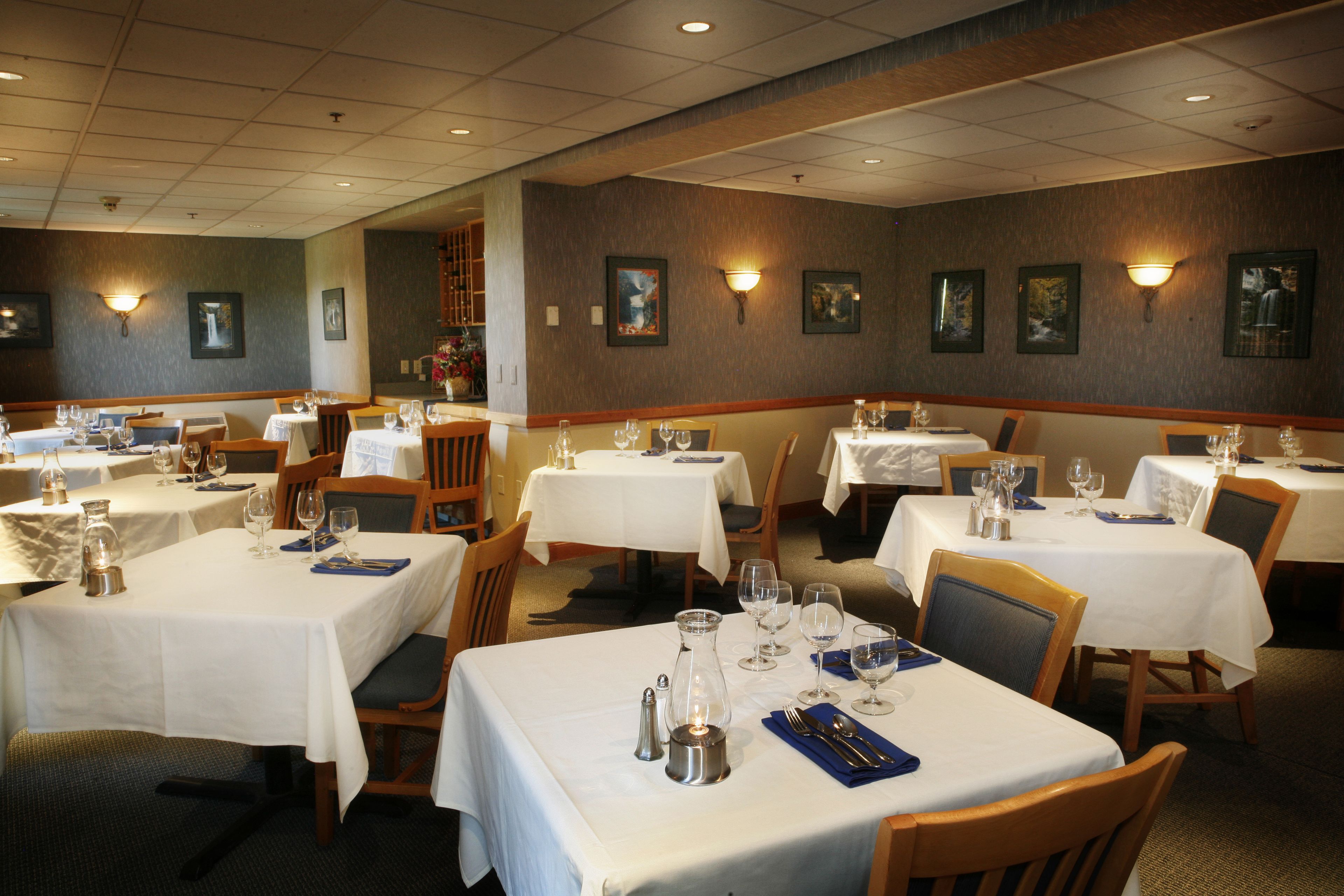 A restaurant with multiple tables set for dining, each with white tablecloths and basic tableware.