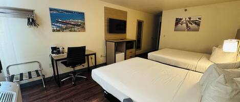 Quarto de hotel com duas camas, uma escrivaninha com cadeira, televisão e janela com vista para uma cidade costeira.