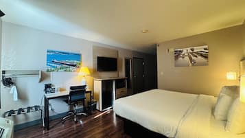 Una habitación de hotel con cama, escritorio, silla, televisor y obras de arte en las paredes.
