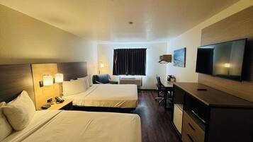 Quarto de hotel com duas camas, uma escrivaninha com cadeira, televisão e janela com cortinas.