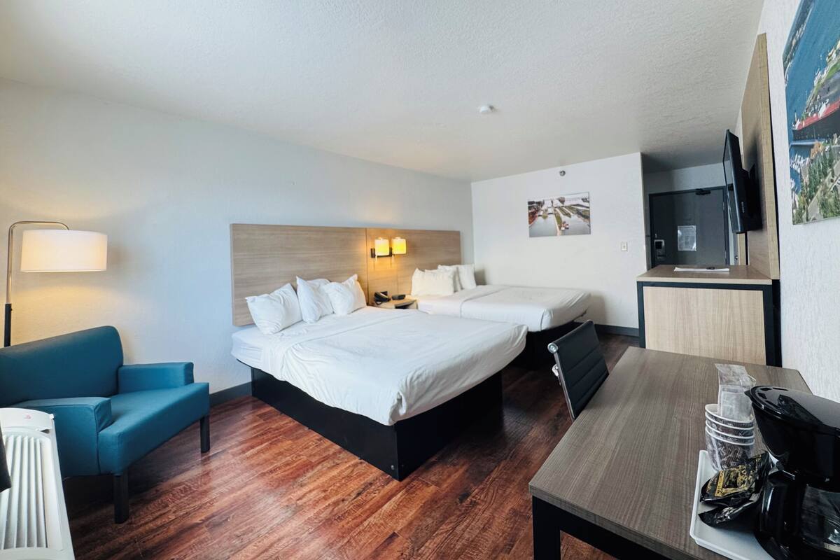A hotel room with a double bed, a desk with a coffee maker, a TV, and a painting on the wall.