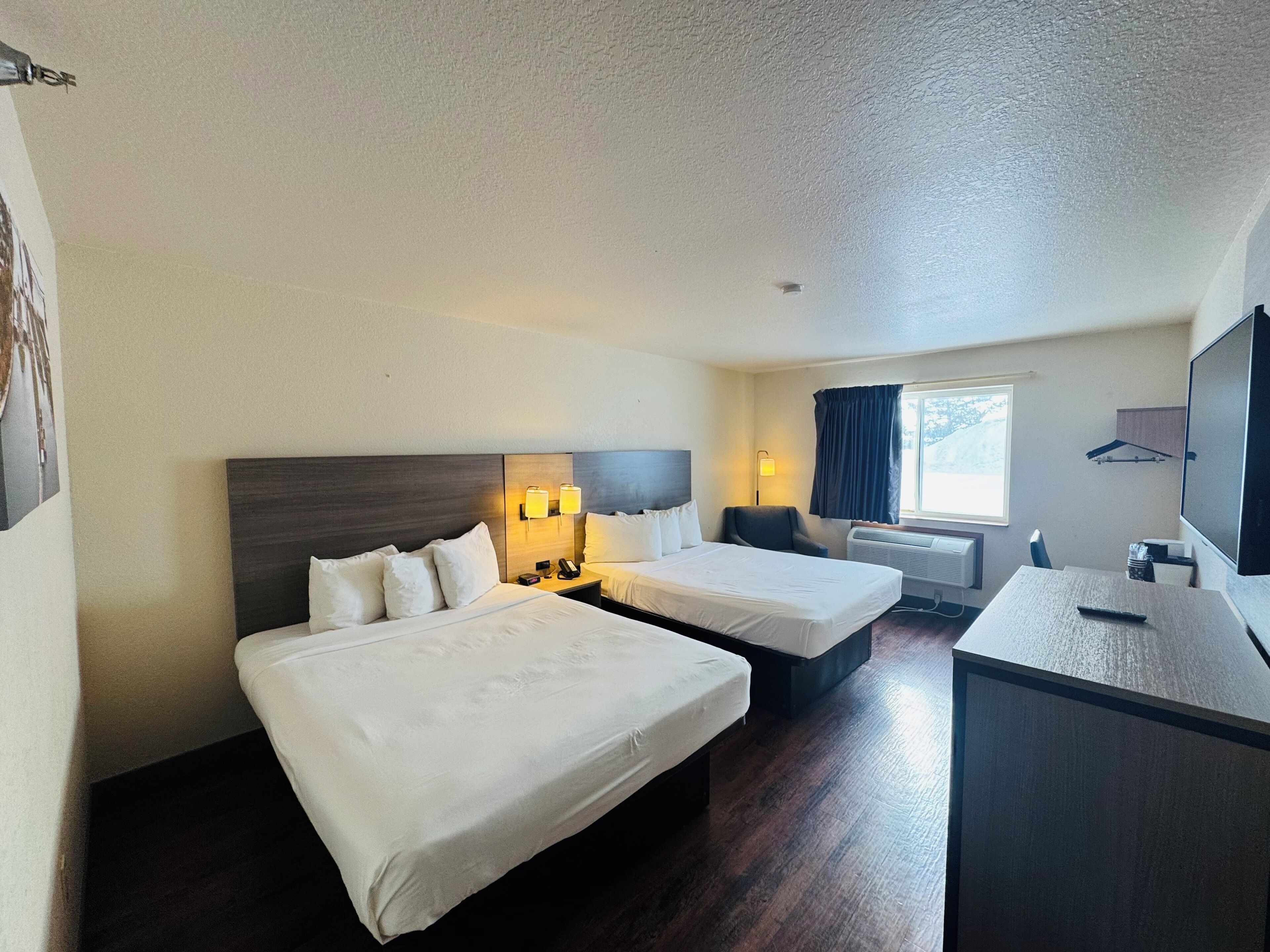 A hotel room with two beds, a desk, a chair, a TV, and a window with curtains.