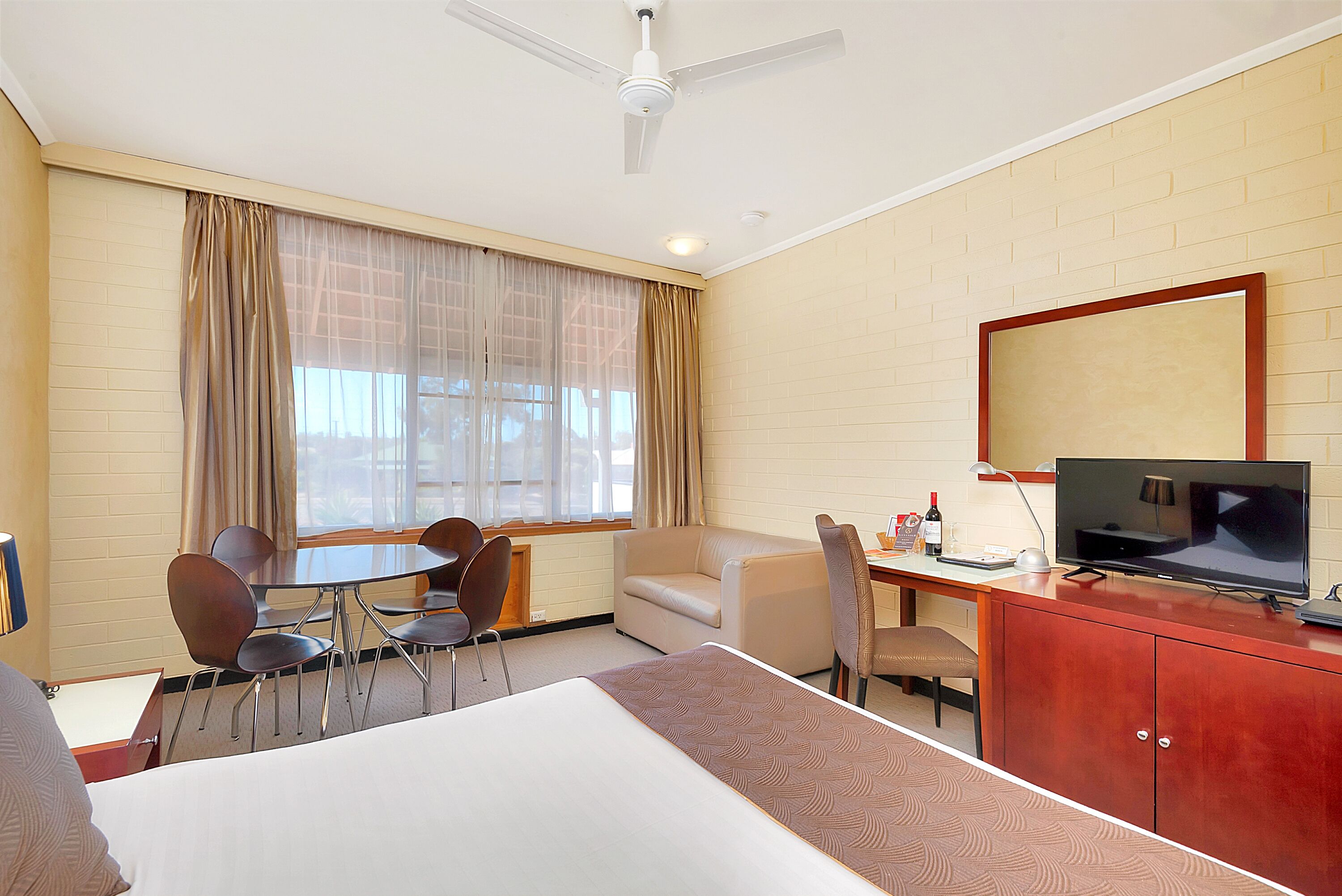 A hotel room with a bed, a desk with a TV, a chair, a sofa, and a dining table.