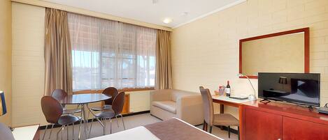 A hotel room with a bed, a desk with a TV, a chair, a sofa, and a dining table.