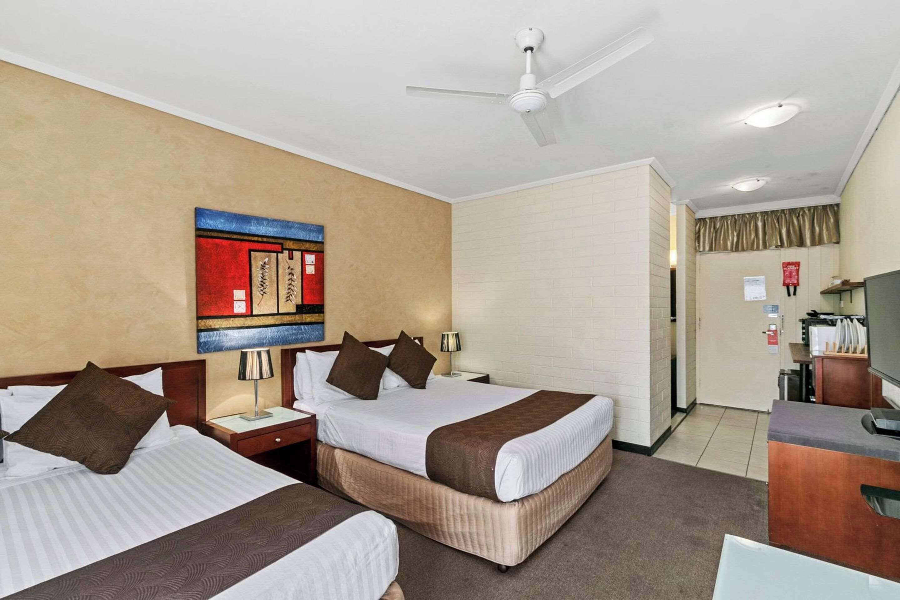 Een hotelkamer met twee bedden, een plafondventilator, een televisie en een bureau met stoel.